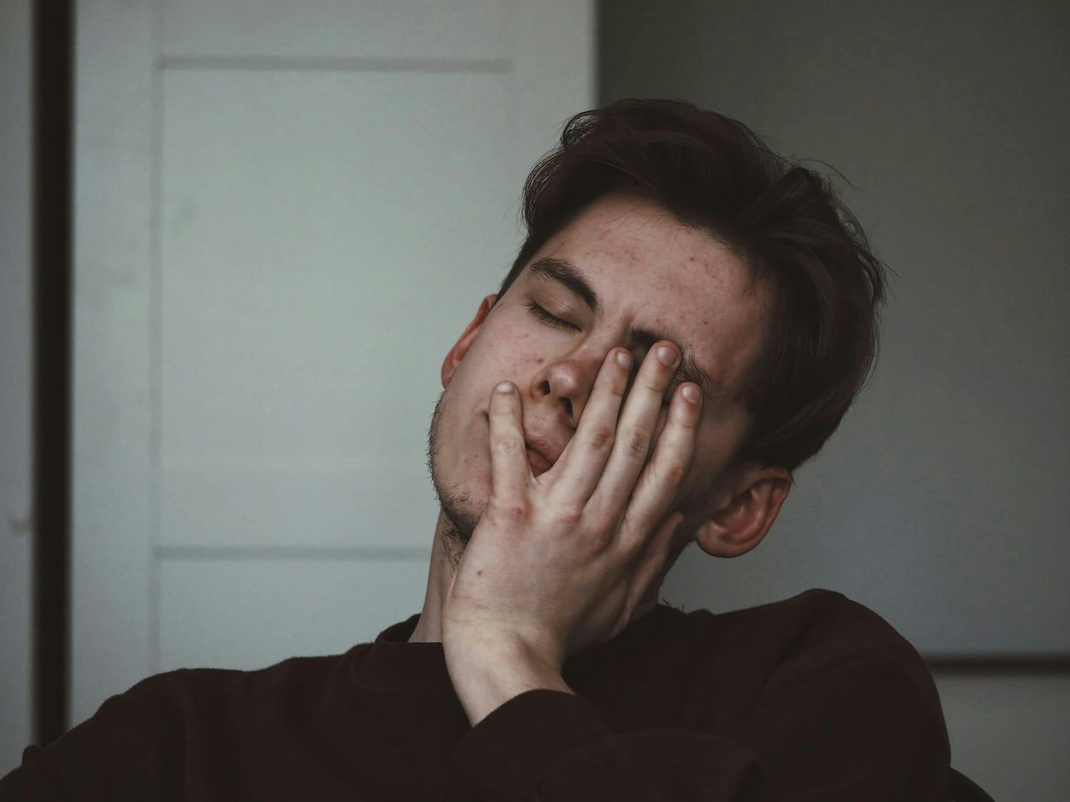 Image shows tired man holding head in exhaustion. 