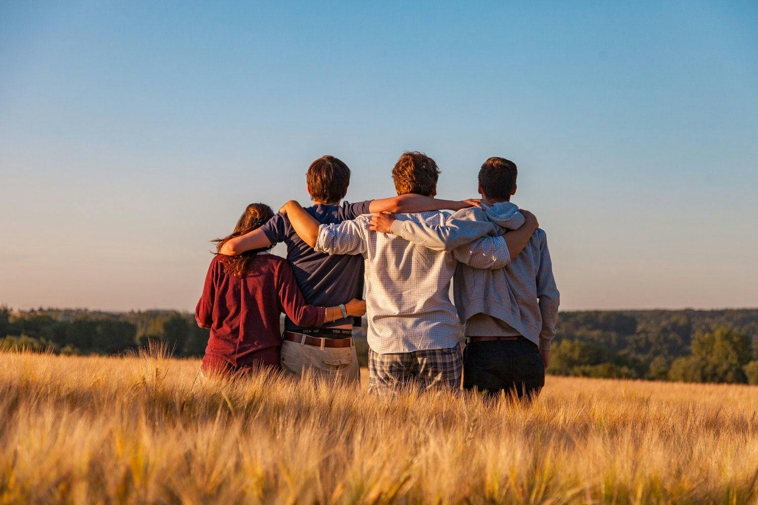Four friends facing away from the camera with their arms around each other