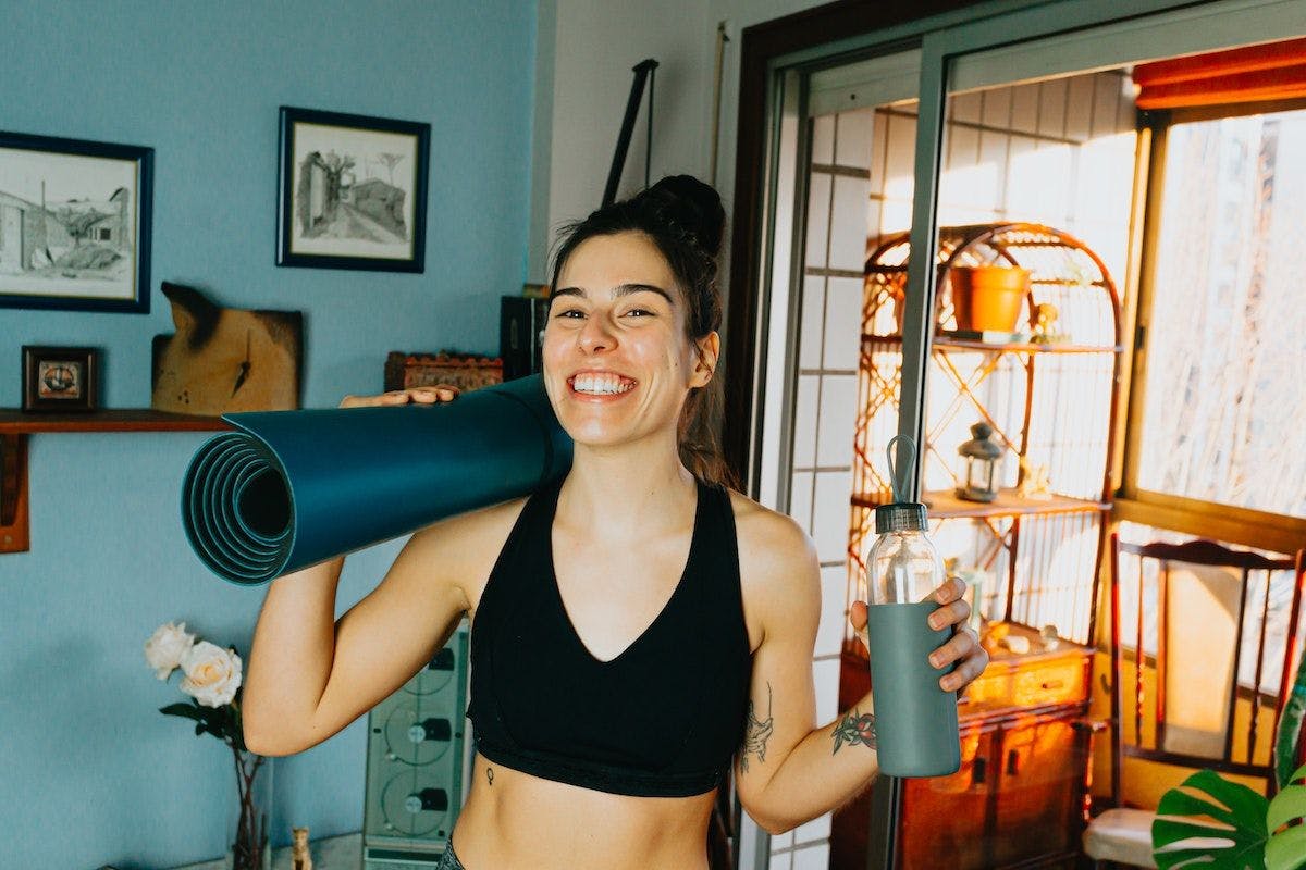 Woman smiling at the camera holding yoga mat and water bottle