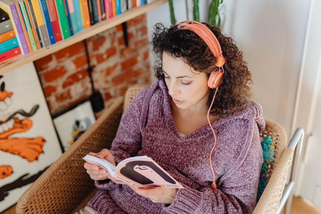 Women with headphones on reading a book