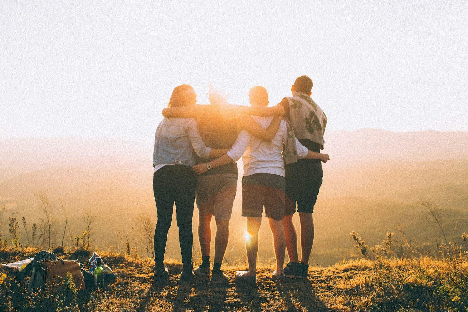 Four people with arms around each other overlooking landscape.