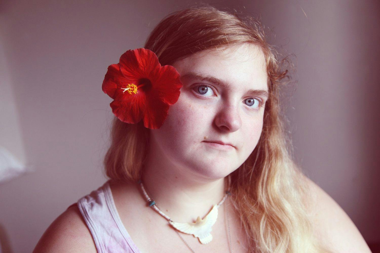 Person looking distantly into camera with a straight face.They have a red flower in their hair. 