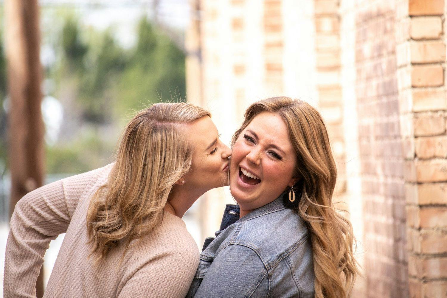 Woman kissing another woman on the cheeks who has a wide smile. 