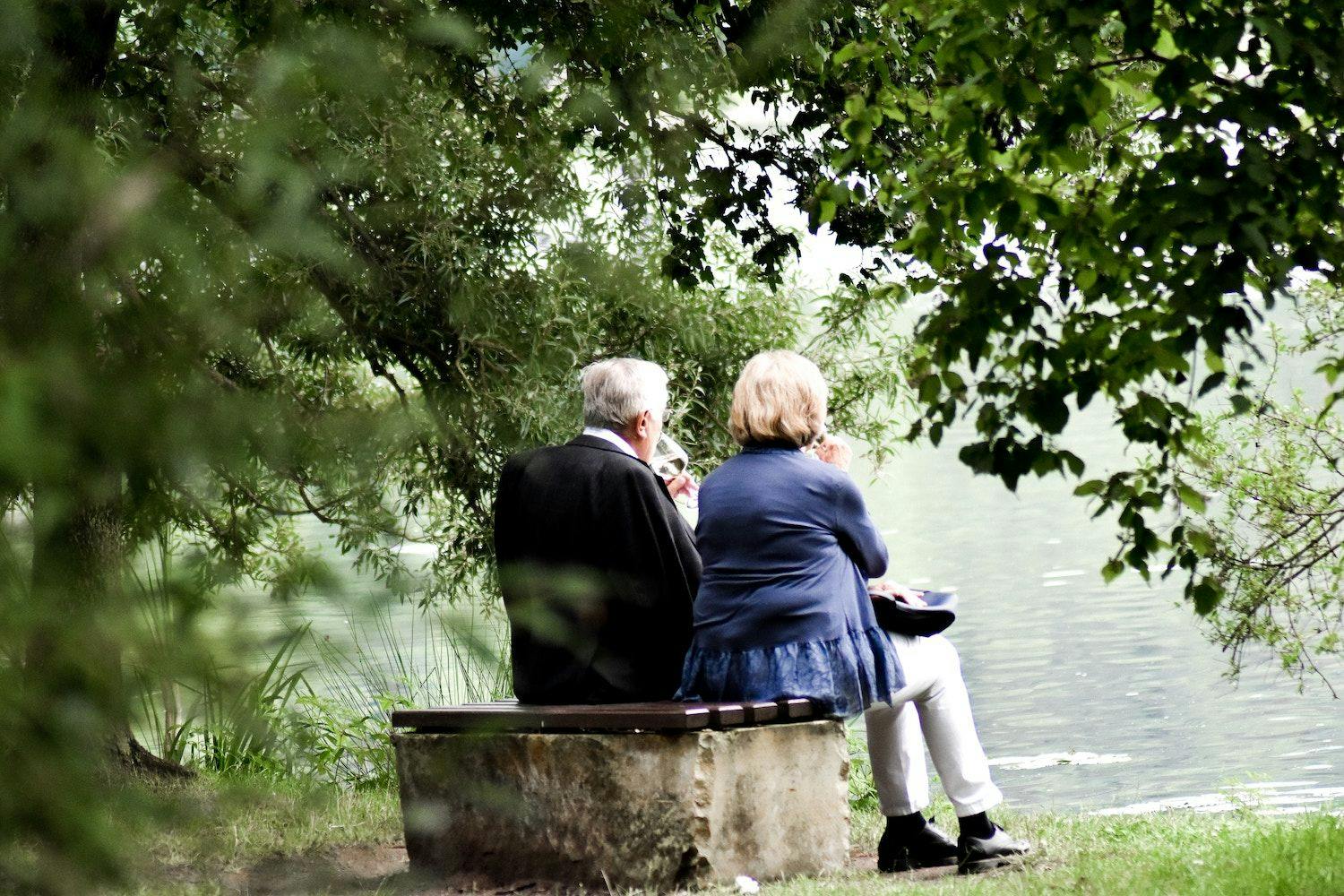 Couple sat on a bench overlooking a lake.