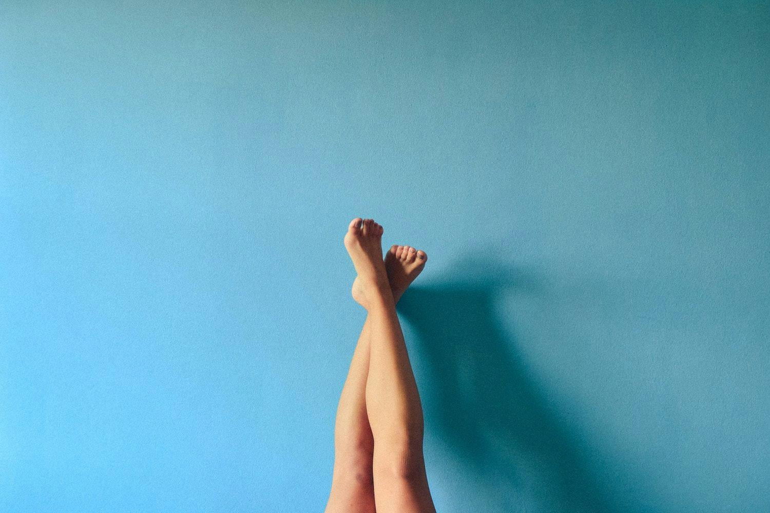 Legs and feet against a blue wall pointing upwards. 