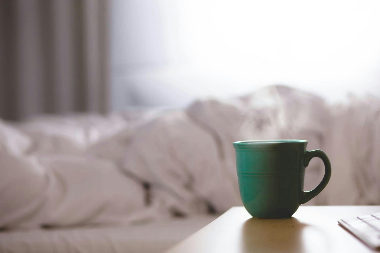 Green mug of tea on a bedside table. 
