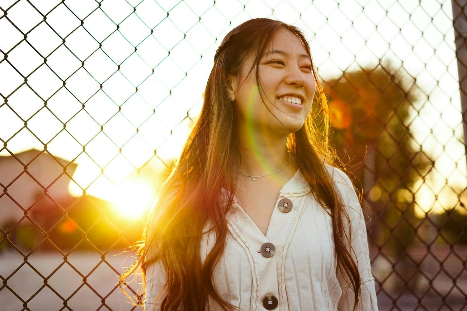 Image shows a girl smiling with the sun setting behind her. 
