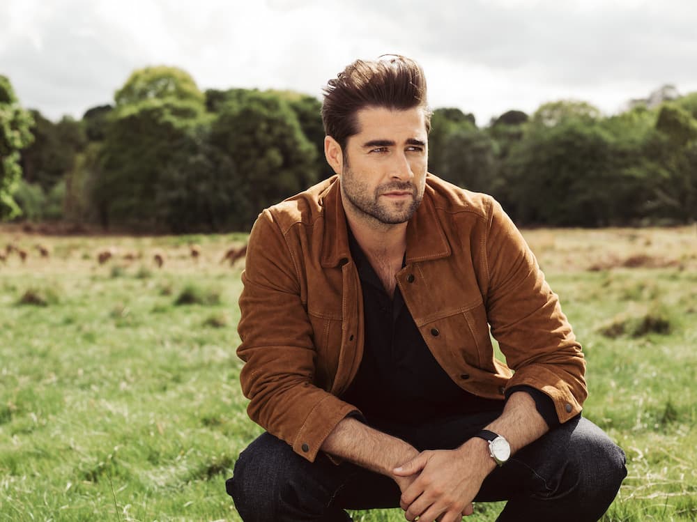 This is a photo of matt crouched down in a field with deer behind him