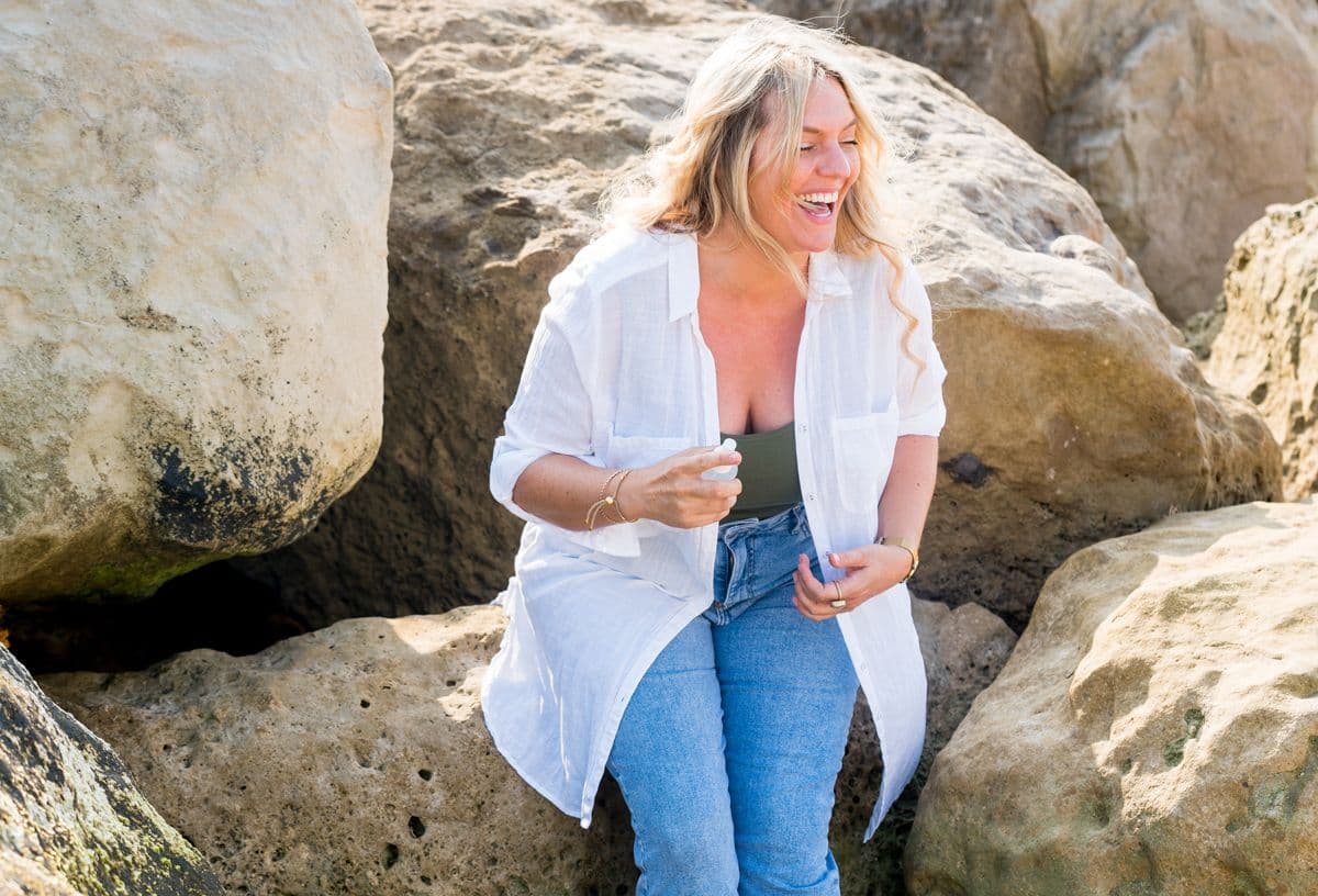Beth standing on the rocks at the beach smiling