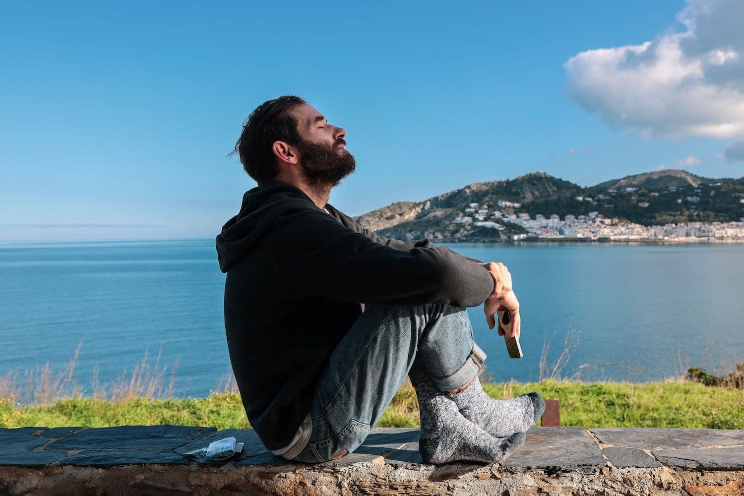 Person sitting on a wall in front of the sea.