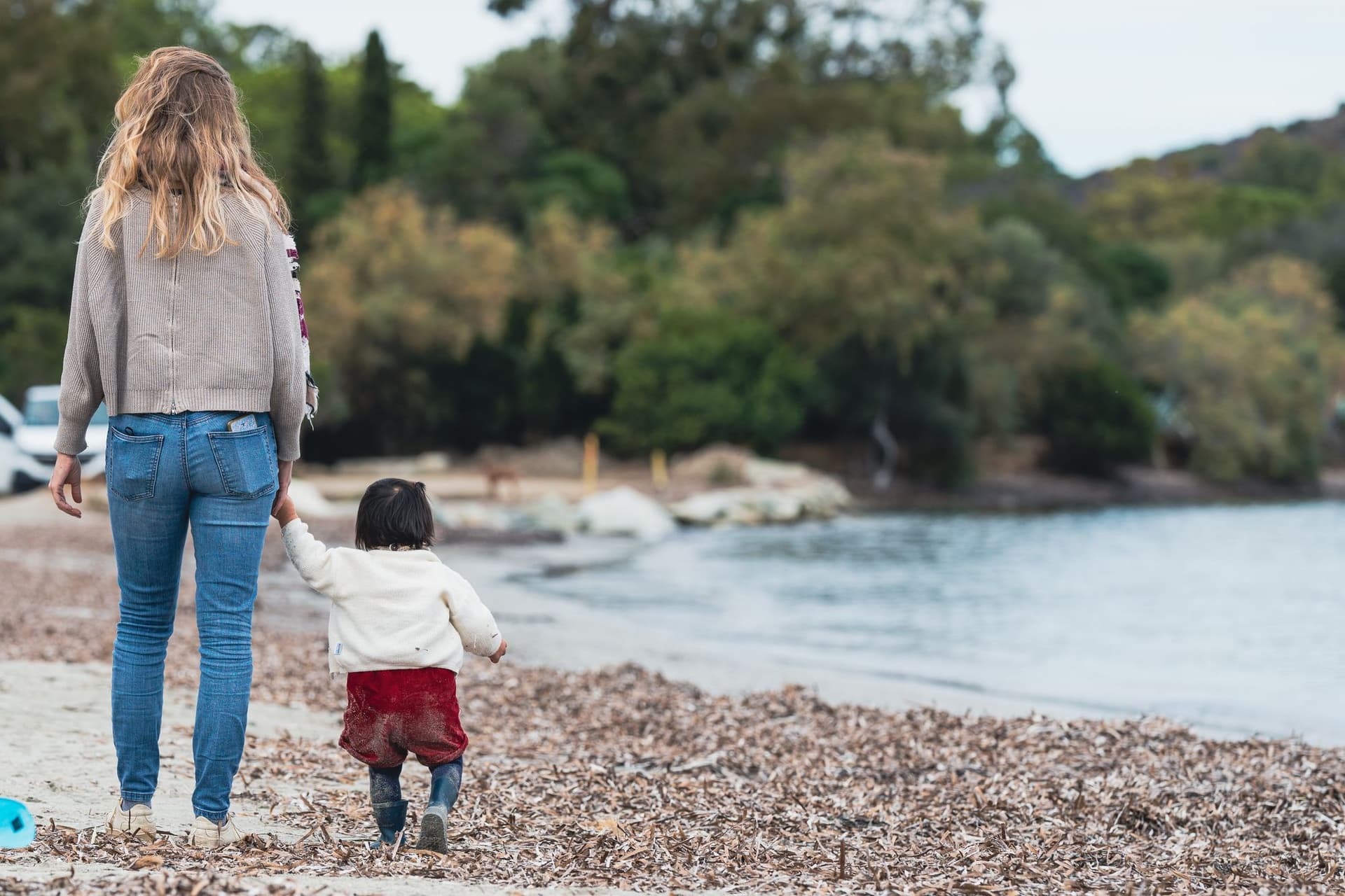 Mum holding hands with child walking along beach