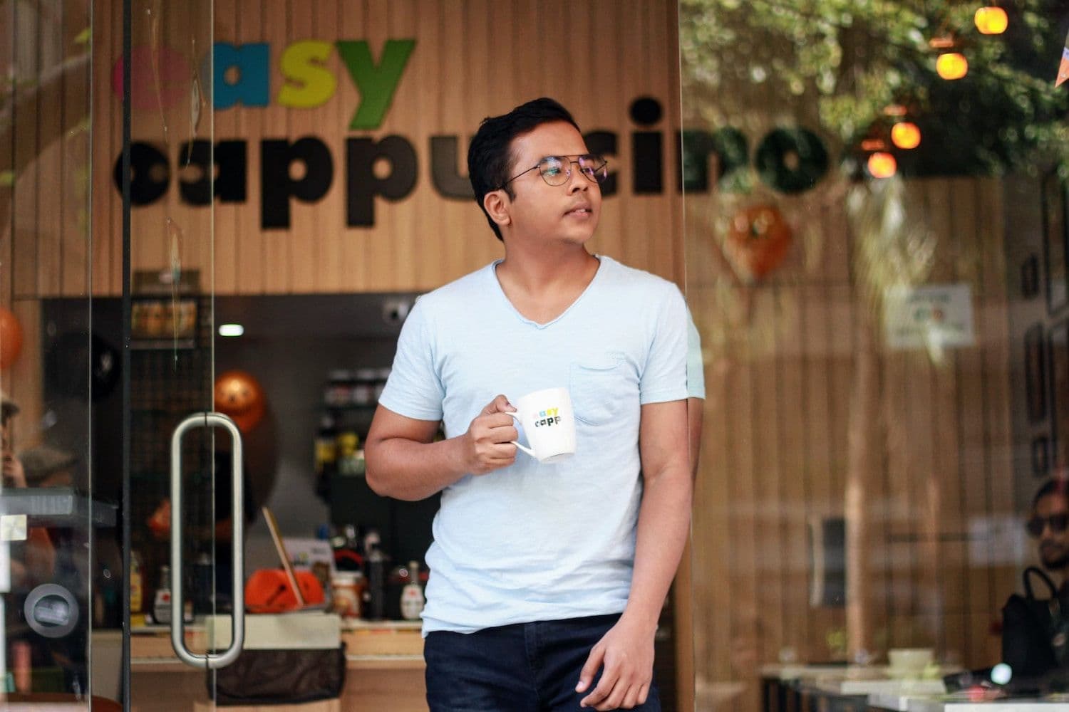 Person holding a drinking mug whilst leaning against a door looking off into the distance.