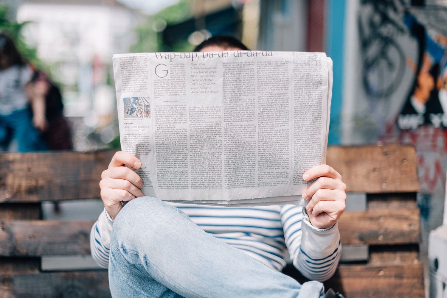 Person sat on a bench reading a newspaper.