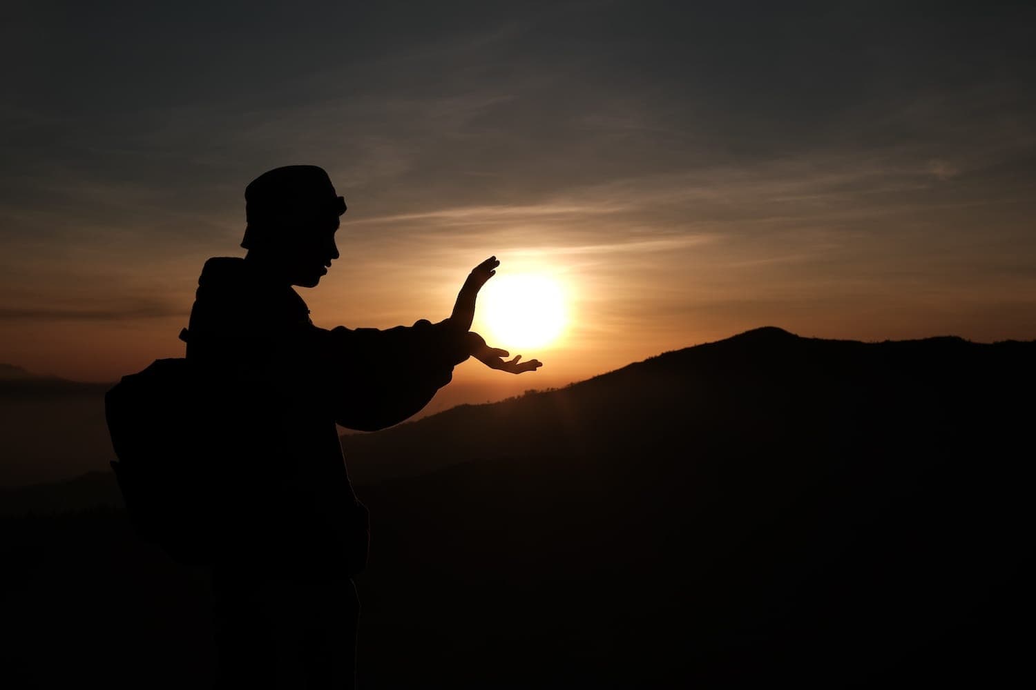 Shadow of a person pretending to hold the sun as it sets in the sky.