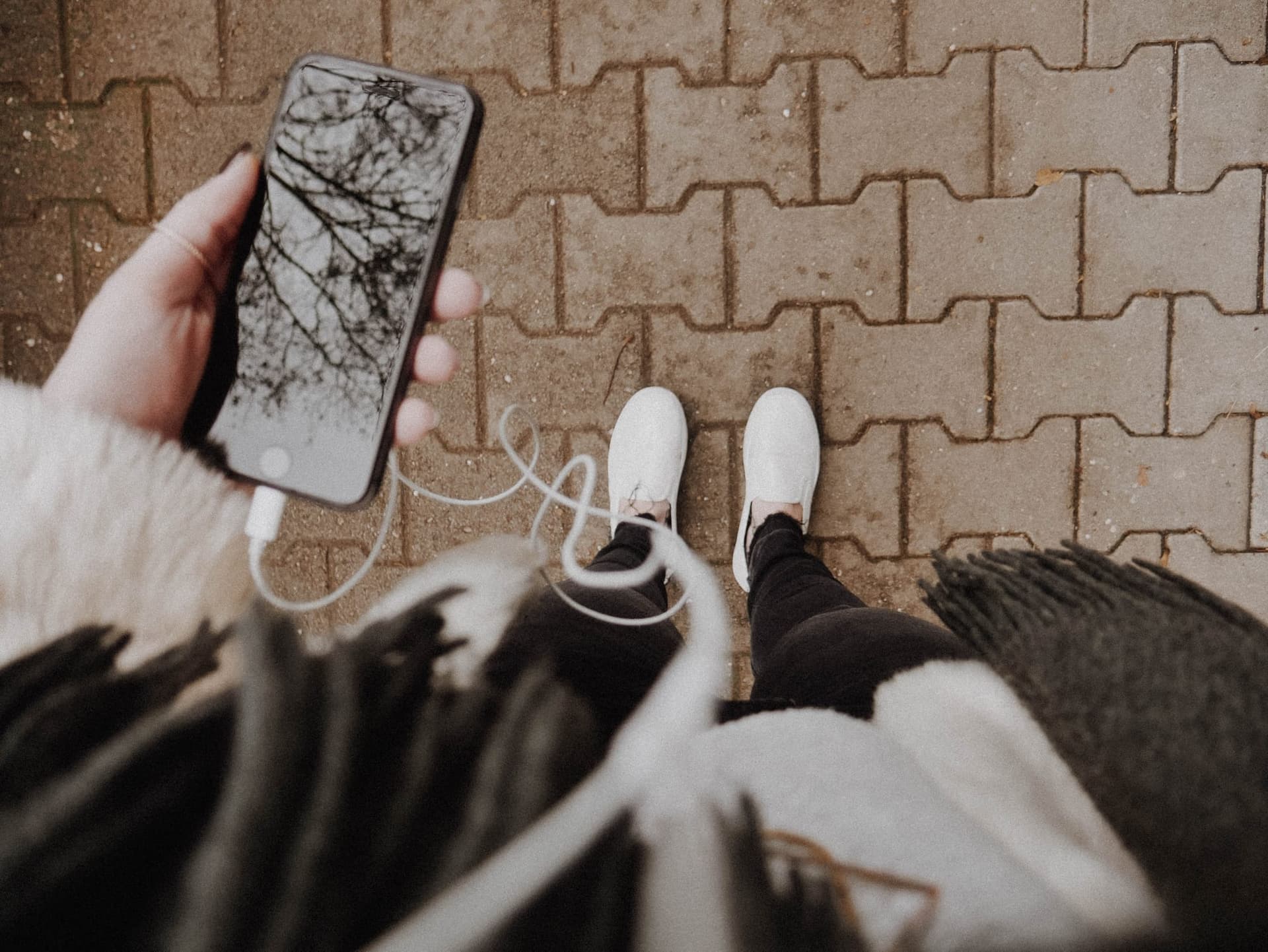 person holding phone and headphones, looking down at feet