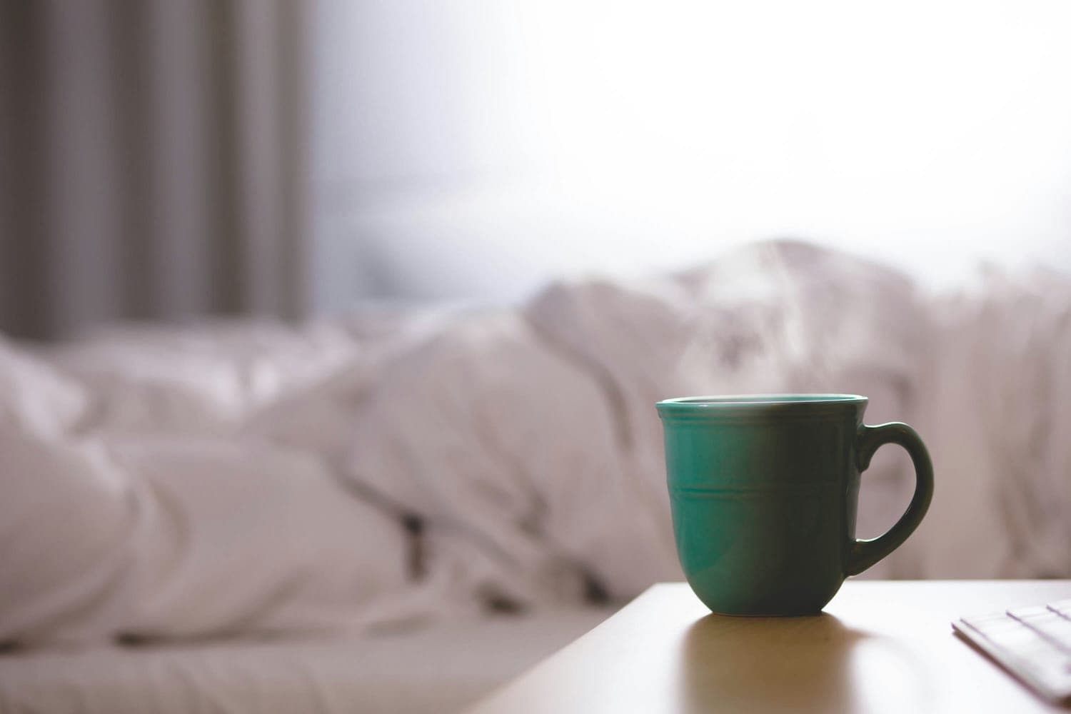 Green mug of tea on a bedside table.