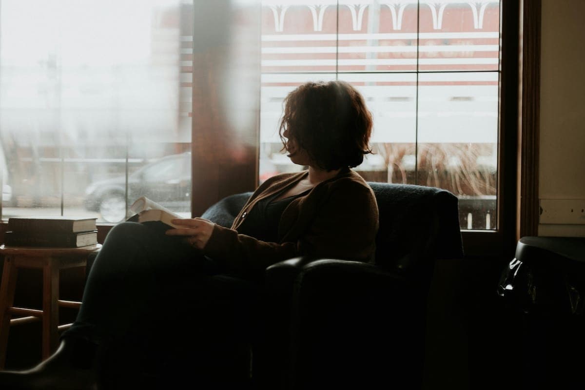 Image shows person sitting in an armchair reading a book.