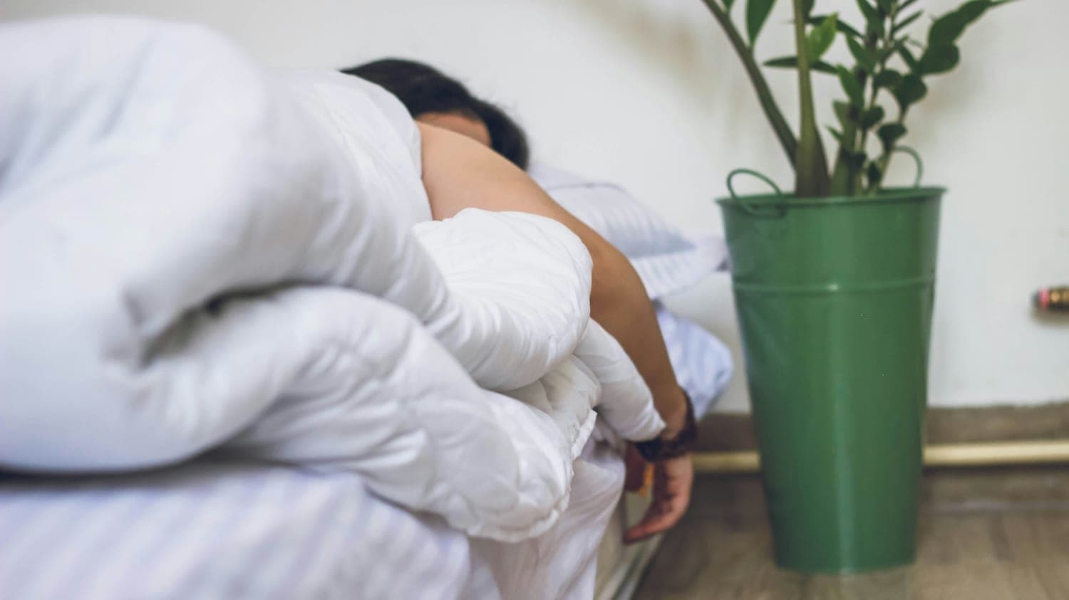 Person sleeping with arm out of bed nestled under white duvet.